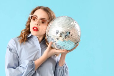 Mavi arka planda disko topu olan güzel, genç ve şık bir kadın.