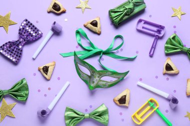 Hamantaschen kurabiyeli karnaval maskesi ve eflatun arka planda Purim tatili için tıkırtılar.