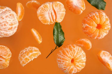 Tatlı soyulmuş mandalinalar ve turuncu arka planda yapraklar uçuşuyor.