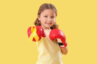 Boks eldivenleri içinde sarı kurdeleli şirin bir kız. Çocukluk kanseri farkındalığı