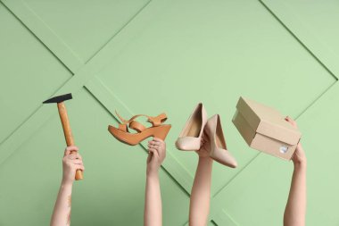 Ayakkabılı kadın eller, yeşil ahşap arka planda kutu ve çekiç. Ayakkabı tamiri kavramı