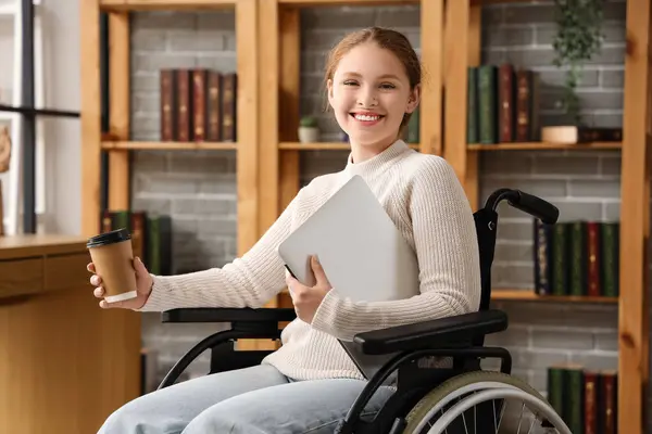 Young redhead woman in wheelchair with laptop and coffee cup at library