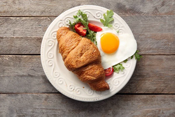 Ahşap zemin üzerinde lezzetli kızarmış yumurta, kruvasan, domates ve roka tabağı.