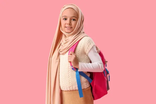 Little Muslim girl in hijab with school backpack on pink background