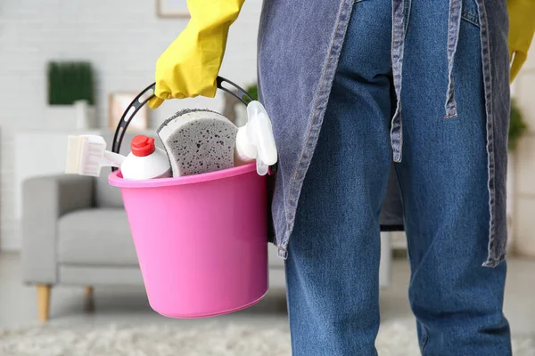 Woman holding bucket with cleaning supplies in living room, closeup