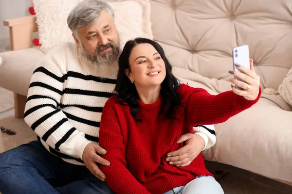 Beautiful mature couple with mobile phone taking selfie at home. Valentine\'s Day celebration