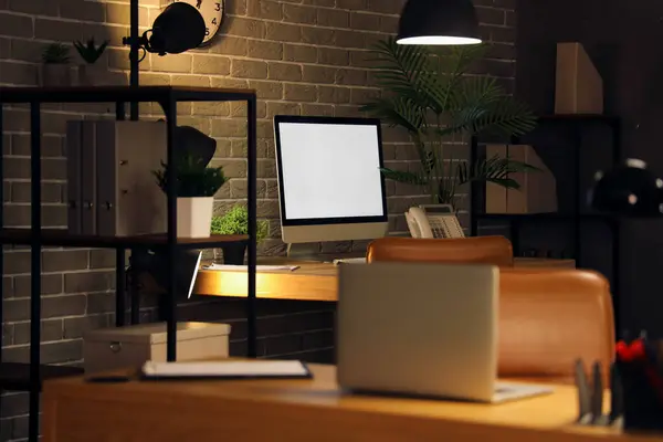 Blank computer monitor on desk in dark office at night