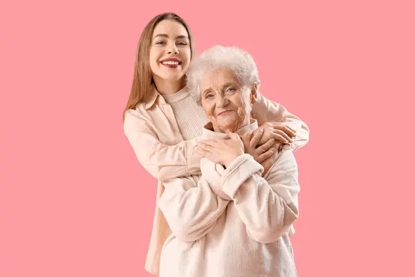 Young woman hugging her grandmother on pink background