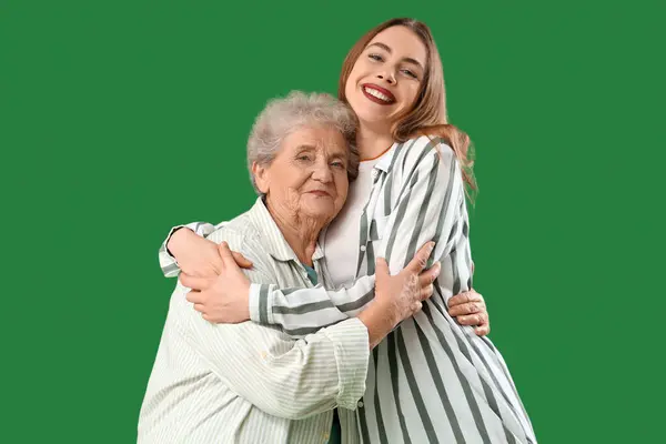 Young woman hugging her grandmother on green background