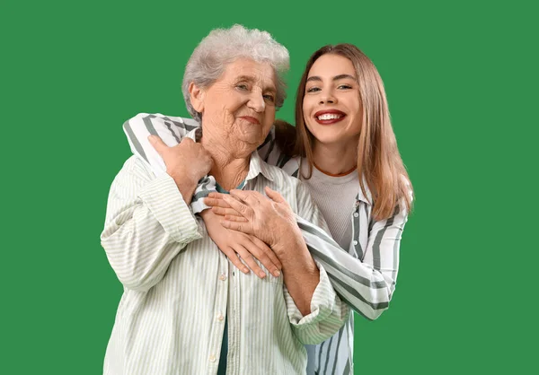 Young woman hugging her grandmother on green background