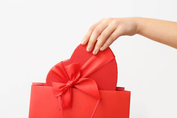 Female hand with paper shopping bag and gift box on white background. Valentine's Day celebration