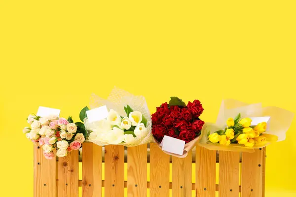 Stand with bouquets of flowers for sale on yellow background