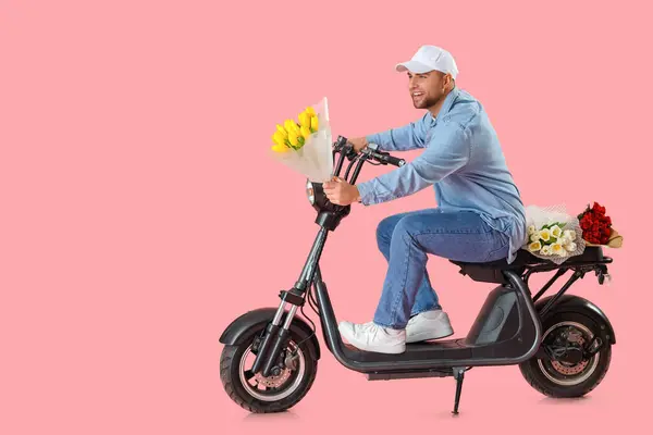 Delivery man with flowers driving scooter on pink background