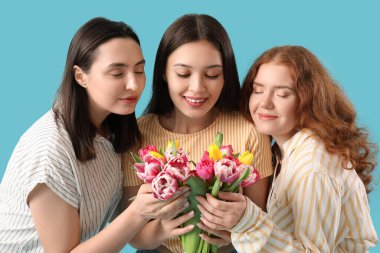 Mavi arka planda güzel lalelerle dolu buketi olan genç kadınlar. Uluslararası Kadınlar Günü