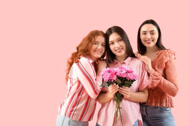 Renkli arka planda pembe kasımpatı çiçekleri olan mutlu genç kadınlar. Uluslararası Kadınlar Günü