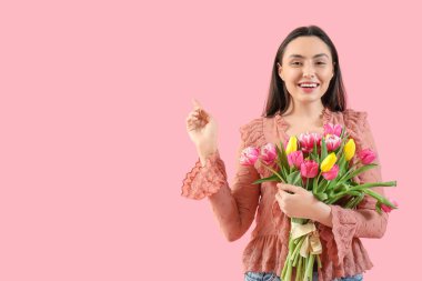 Güzel lalelerle dolu buketi olan genç bir kadın pembe arka plandaki bir şeyi işaret ediyor. Uluslararası Kadınlar Günü