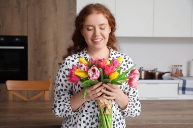 Mutfakta bir buket güzel lalesi olan mutlu genç bir kadın. Uluslararası Kadınlar Günü