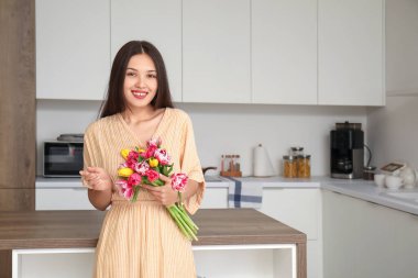 Mutfakta bir buket güzel lalesi olan genç Asyalı kadın. Uluslararası Kadınlar Günü