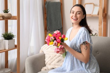 Evdeki kanepede güzel lalelerle dolu buketi olan mutlu genç bir kadın. Uluslararası Kadınlar Günü