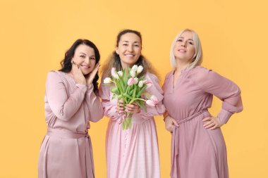 Sarı arka planda bir buket güzel lalesi olan olgun kadınlar. Uluslararası Kadınlar Günü