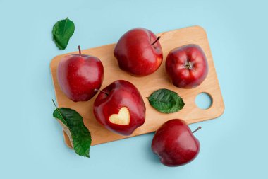 Ahşap tahta tahta tahta tahta üzerinde oyulmuş kalp ve mavi arka plan yaprakları olan kırmızı elmalar.