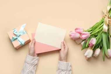 Boş kartı olan kadın elleri, hediye kutusu ve sarı arka planda bir buket güzel lale. Uluslararası Kadınlar Günü
