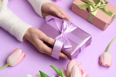 Hediye kutuları ve mor arka planda güzel laleleri olan kadın elleri. Uluslararası Kadınlar Günü