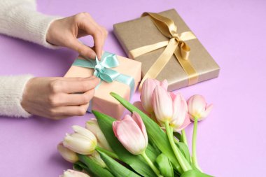 Hediye kutularıyla kadın elleri ve mor arka planda bir buket güzel laleler. Uluslararası Kadınlar Günü
