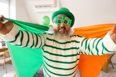 Aziz Patrick Günü 'nde evinde İrlanda bayrağı taşıyan şapkalı olgun bir adam.