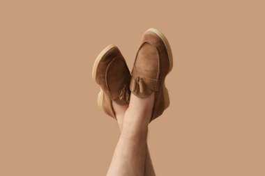 Kahverengi arka planda şık ayakkabılı genç adam bacakları.