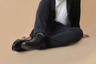 Kahverengi arka planda siyah şık ayakkabılı genç adam.