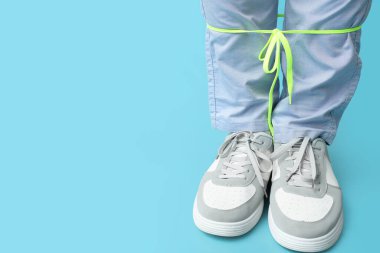 Mavi arka planda bağcıkları olan şık spor ayakkabılı genç adamın bacakları.