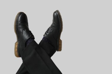 Gri arka planda siyah şık ayakkabılı genç adamın bacakları.