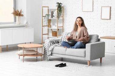 Evdeki kanepede sopayla glukofon çalan mutlu olgun bir kadın.