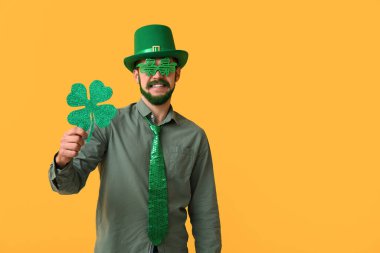 Leprikon şapkalı ve yeşil sakallı, sarı arka planda yonca tutan dekoratif gözlüklü genç adam. Aziz Patrick Günü kutlaması