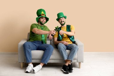 Yeşil sakallı, leprikon şapkalı genç adamlar ellerinde bira şişeleri ve bej duvarın yanındaki kanepede oturuyorlar. Aziz Patrick Günü kutlaması