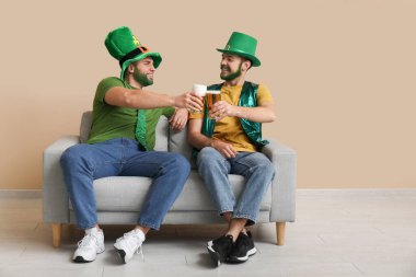 Yeşil sakallı, leprikon şapkalı genç adamlar ellerinde bira bardakları ve bej duvarın yanındaki kanepede oturuyorlar. Aziz Patrick Günü kutlaması