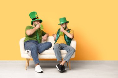 Yeşil sakallı, leprikon şapkalı genç adamlar ellerinde bira bardakları ve sarı duvarın yanındaki kanepede oturuyorlar. Aziz Patrick Günü kutlaması