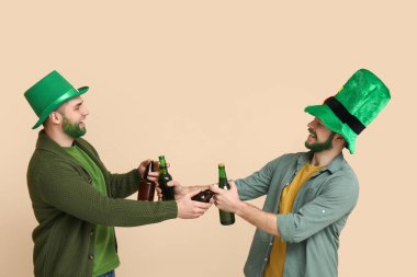 Yeşil sakallı, leprikon şapkalı genç adamlar bej arka planda bira şişeleri tutuyorlar. Aziz Patrick Günü kutlaması