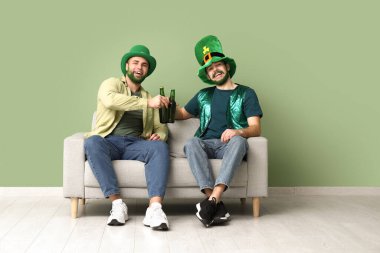 Yeşil sakallı ve yeşil sakallı mutlu genç adamlar ellerinde bira şişeleri ve yeşil duvarın yanındaki kanepede oturuyorlar. Aziz Patrick Günü kutlaması