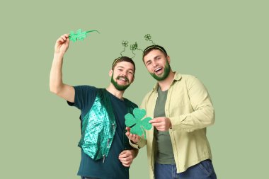 Yeşil sakallı genç adamlar yeşil arka planda yonca tutuyorlar. Aziz Patrick Günü kutlaması