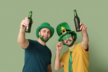 Yeşil sakallı cüce şapkalı genç adamlar yeşil arka planda bira şişeleri taşıyorlar. Aziz Patrick Günü kutlaması