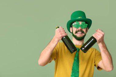 Leprikon şapkalı, yeşil sakallı ve yeşil arka planda bira şişeleri tutan yonca şeklinde dekoratif gözlüklü genç bir adam. Aziz Patrick Günü kutlaması