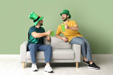 Yeşil sakallı, leprikon şapkalı genç adamlar ellerinde bira bardakları ve yeşil duvarın yanındaki kanepede oturuyorlar. Aziz Patrick Günü kutlaması