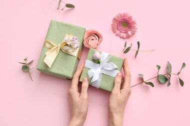 Hediye kutuları ve pembe arka planda güzel çiçekler olan kadın elleri. Uluslararası Kadınlar Günü