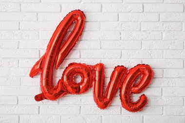 Aşk kelimesi beyaz tuğla duvarda asılı duran balonlardan yapılmış, yakın plan. Sevgililer Günü kutlaması