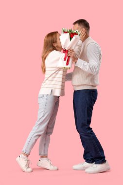 Orta yaşlı çift pembe arka planda bir buket çiçekle yüzlerini kapatıyor. Uluslararası Kadınlar Günü