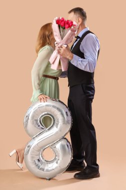 Bej arka planda 8 şeklinde balon ve buketi olan orta yaşlı bir çift. Uluslararası Kadınlar Günü