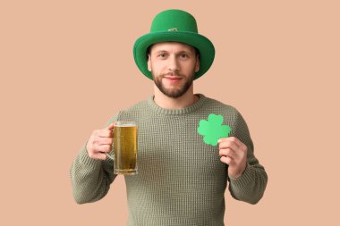Kahverengi arka planda bir bardak bira ve yoncayla cüce şapkalı genç adam. Aziz Patrick Günü kutlaması