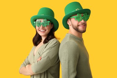 Leprikon şapkalı ve sarı arka planda yonca şeklinde dekoratif gözlüklü güzel bir çift. Aziz Patrick Günü kutlaması